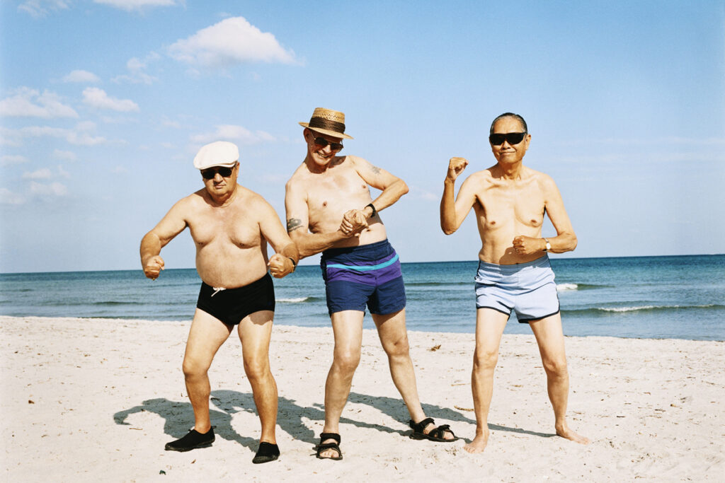 Three Senior Men in Swimming Trunks Stand on the Beach Flexing Their Muscles Passion Dome